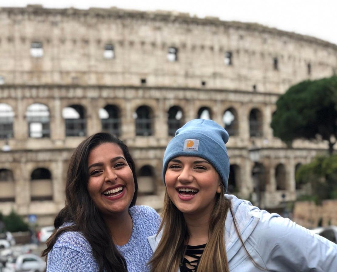 Two students smile together outside of the Coliseum in Rome.